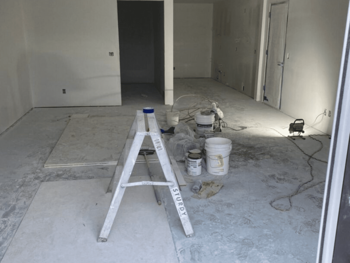 A ladder and buckets in an unfinished room.